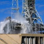 A large amount of water cascades over the edges of the gray mobile launcher at NASA's Kennedy Space Center. Droplets of water also spray up through the air, creating a mist.
