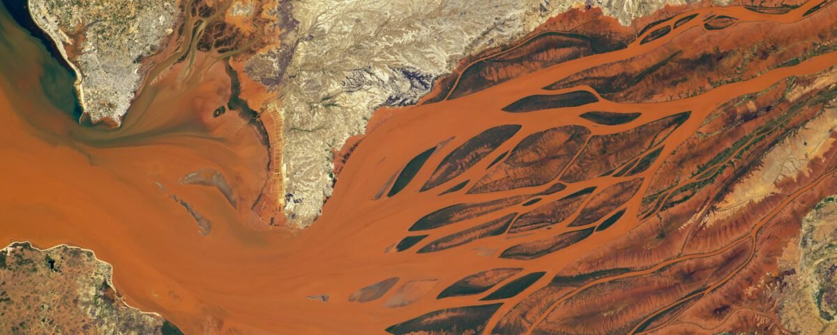 The waters of the Betsiboka River Delta, as seen from the International Space Station, are a vibrant orange. From left to right, the river branches off into many pathways, looking almost like the roots of a tree.