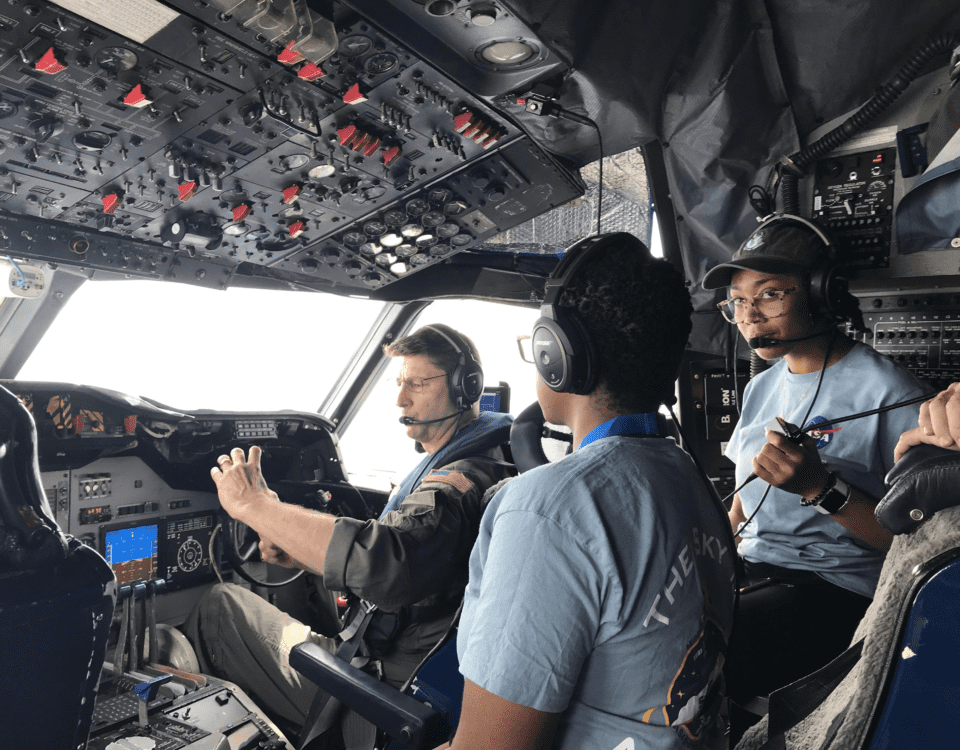 Students of the 2022 SaSa class stand in a cockpit, learning from a NASA airman as part of a training module.